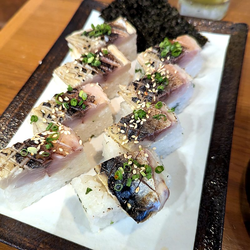 Pressed mackerel sushi topped with sesame and green onion