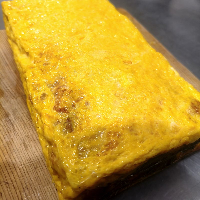A whole block of freshly made Japanese rolled omelette on a wooden board