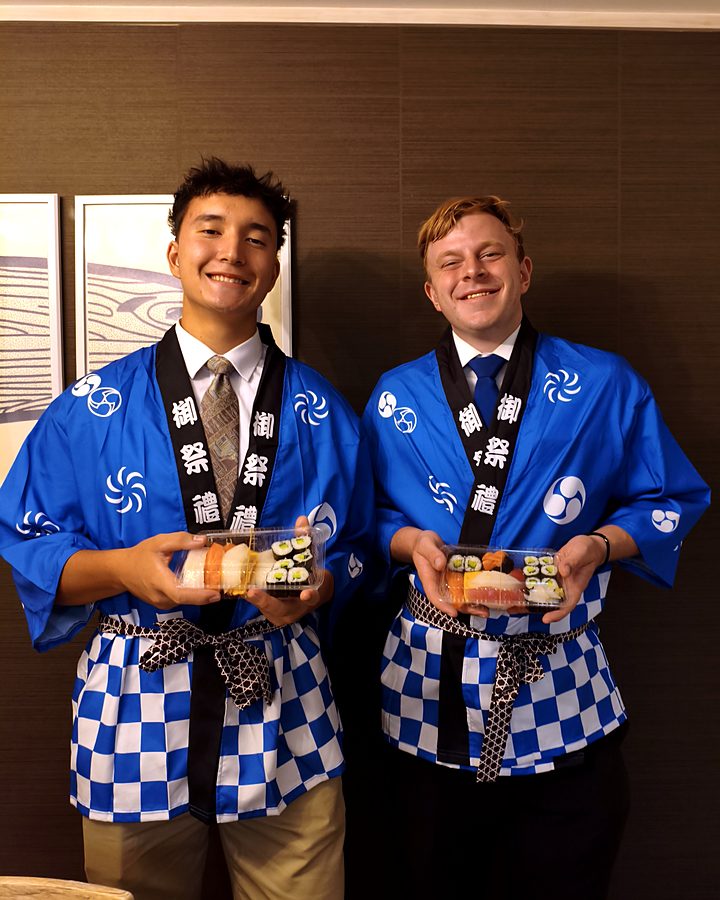 Two guests in blue happi coats holding the sushi they made