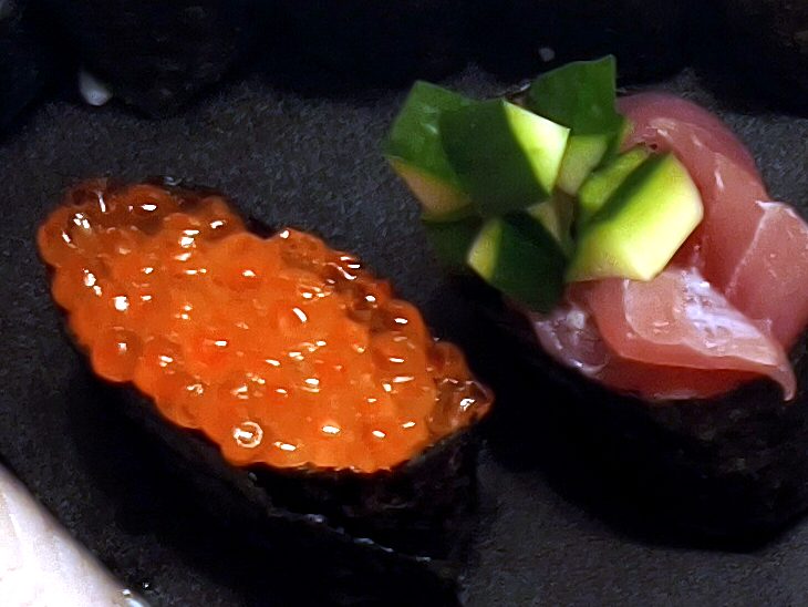 Two gunkan sushi topped with salmon roe and with tuna and cucumber